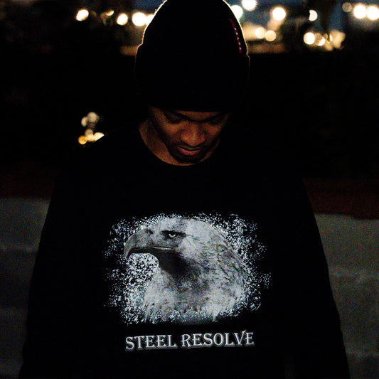 Person wearing a black longsleeve with an eagle design and 'Steel Resolve' text at night.